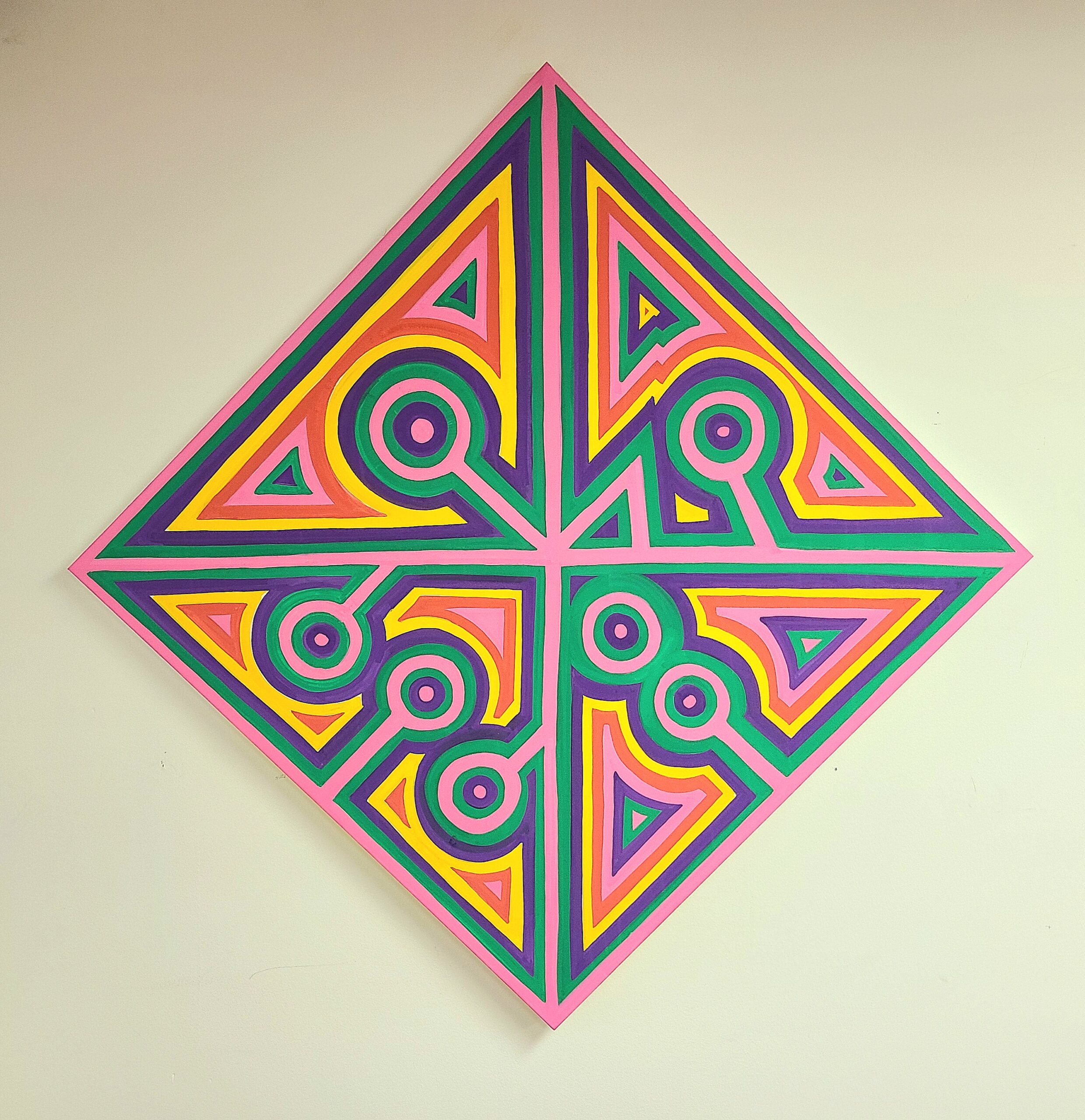 The image shows a piece of artwork by Cody Aguirre. It is a diamond-shaped canvas divided into symmetrical sections, each filled with vibrant and contrasting colors such as pink, yellow, green, and purple. The design features a combination of geometric patterns, including triangles and circles, with circular patterns at the tips of the diamond.