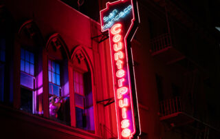 A drag performer sings through the windows of CounterPulse, with it's neon lights illuminating the building